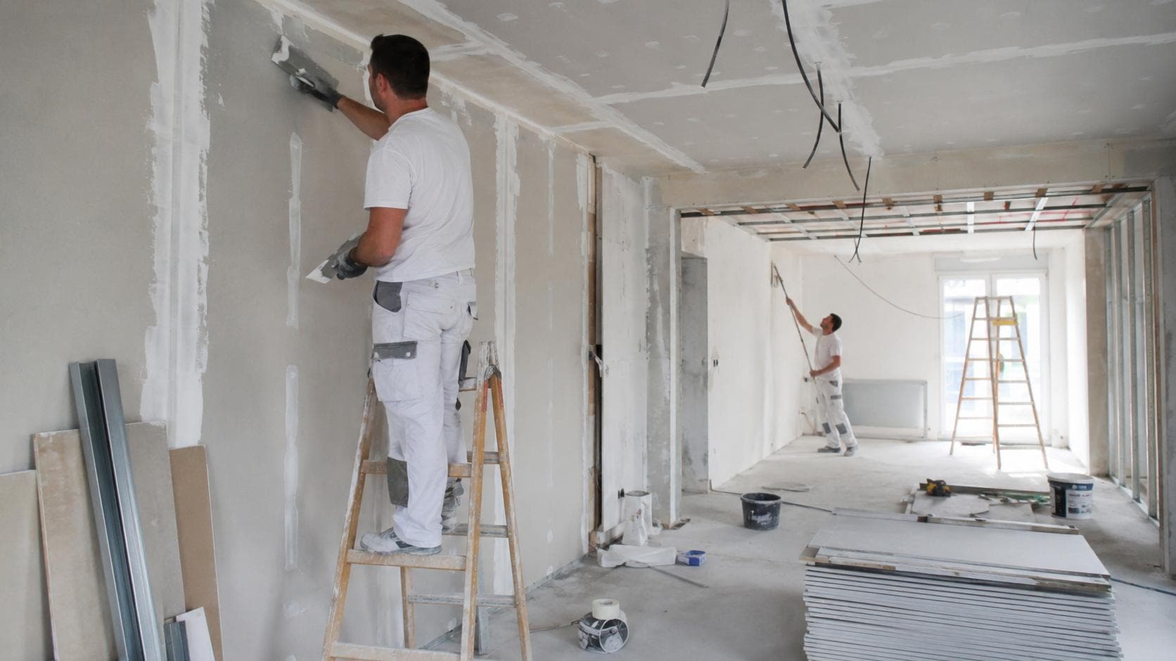 Plaquiste posant une plaque de plâtre sur une ossature métallique, chantier intérieur.